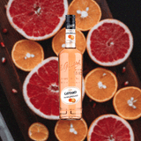 Bottle of Giffard Pamplemousse Liqueur over backdrop of table lined with citrus fruits.