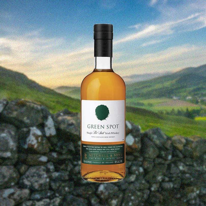Bottle of Green Spot Irish Whiskey over scenic backdrop of a stone wall and green valley