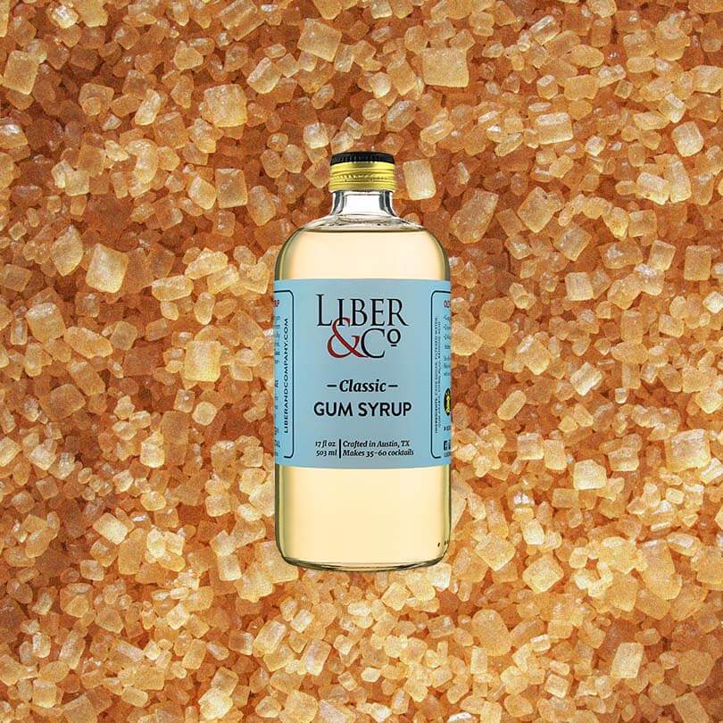 Bottle of Liber & Co. Classic Gum Syrup over backdrop of light sugar candies.