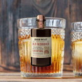 Bottle of High West Old Fashioned Barrel Finished Cocktail, over blurred backdrop of cocktails sitting with a wooden background.