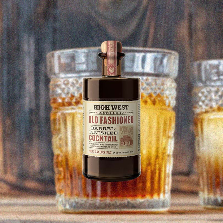 Bottle of High West Old Fashioned Barrel Finished Cocktail, over blurred backdrop of cocktails sitting with a wooden background.