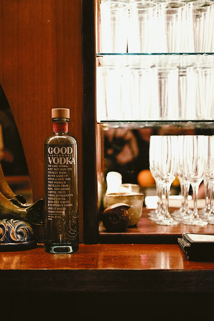 Bottle of Good Vodka, next to lighted bar stocked with various glasses.