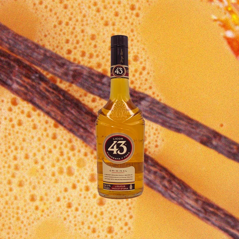 Bottle of Licor 43 Spanish Liqueur, over close up orange colored cocktail garnished with spices.