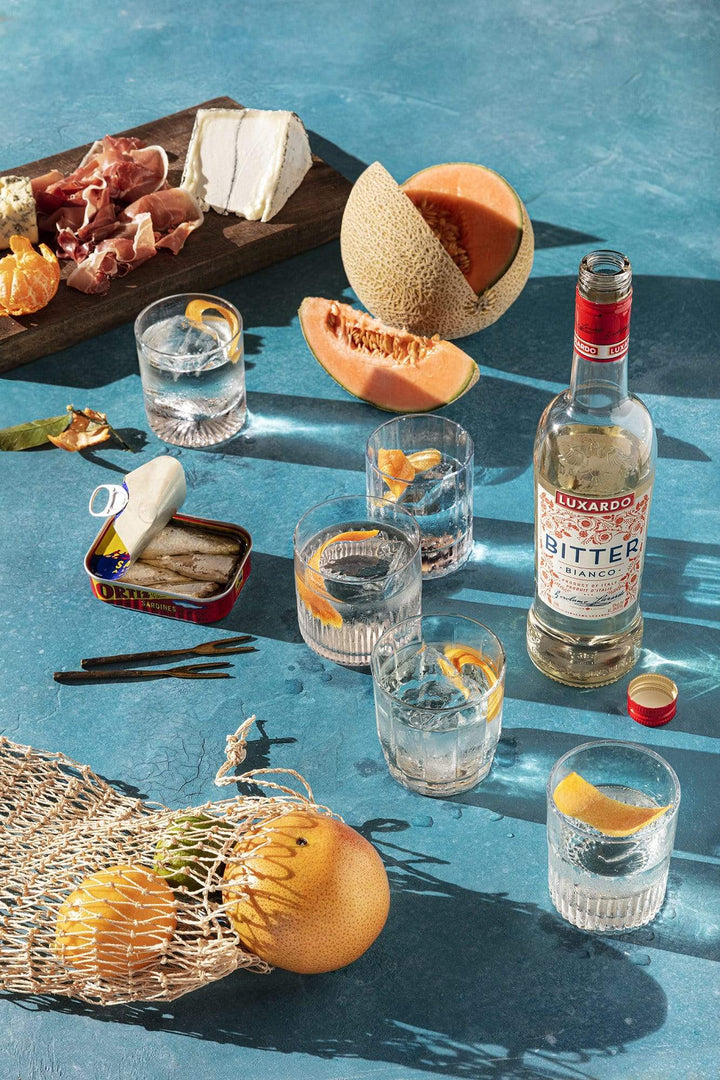 Tablescape of cantaloupe, cocktails, cheese and meat board and sardines.