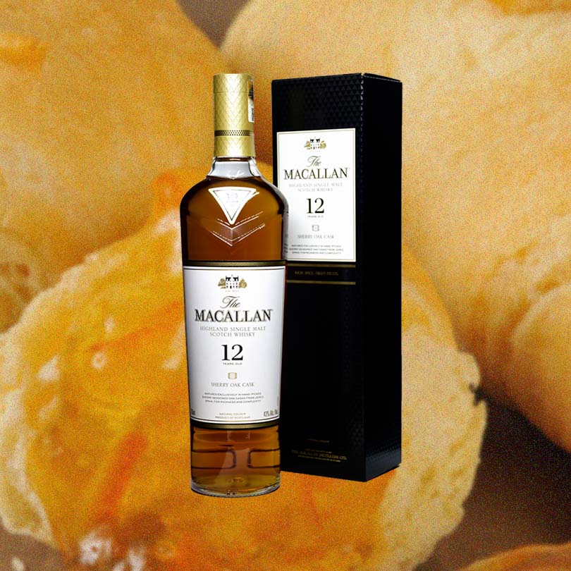 Macallan 12 Year Old Sherry Cask Single Malt Scotch Whisky and accompanying box against a background of fresh baked biscuits