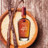 Bottle of Maker's Mark 46 Bourbon, over blurred background of bowl filled with grain and vanilla beans on a wooden table.