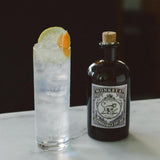 A tall cocktail garnished with fruit on a counter top next to a Monkey 47 bottle.