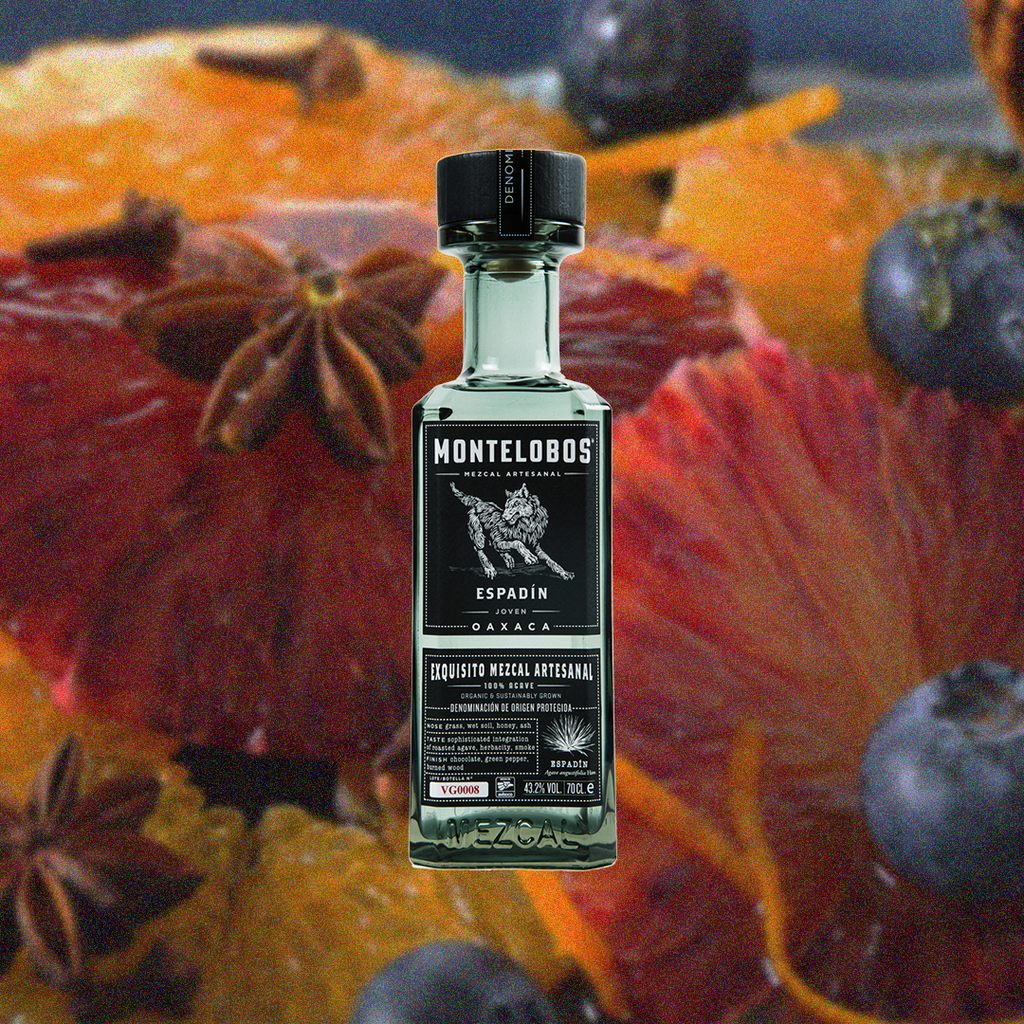 Bottle of Montelobos Espadin Mezcal Joven over backdrop of spices, fruits and berries.