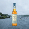 Bottle of Oban Single Malt Scotch Whisky Little Bay Small Cask over backdrop of sailboats anchored in the sea near the shore.