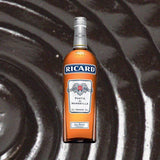 Bottle of Ricard Pastis de Marseille Aperitif over dark black liquorice looking backdrop.