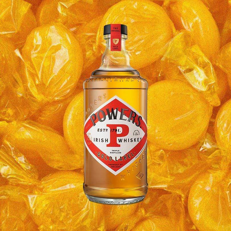 Bottle of Powers Gold Label Irish Whiskey over backdrop of wrapped butterscotch candies.