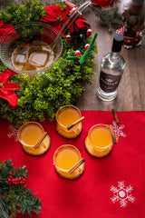 Bottle of RIGHT Gin on wooden table, with holiday decor and four drinks garnished with cinnamon.
