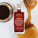 Bottle of Roots Rakomelo Sweet Liqueur, a jar of honey, and honeycomb covered in honey.