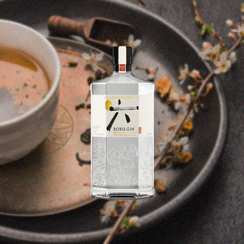 Bottle of Roku Gin over backdrop of a pot, a bowl with liquid and a small branch with white flowers.