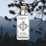 Bottle of Roots Chios Mastic Liqueur over a backdrop image of a pine tree and mountains.