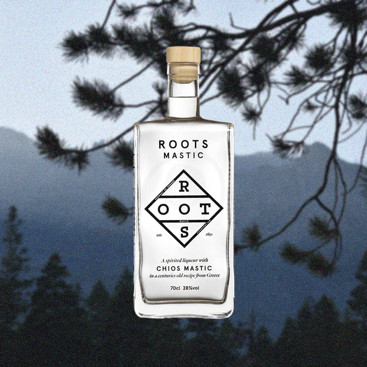 Bottle of Roots Chios Mastic Liqueur over a backdrop image of a pine tree and mountains.
