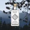Bottle of Roots Chios Mastic Liqueur over a backdrop image of a pine tree and mountains.