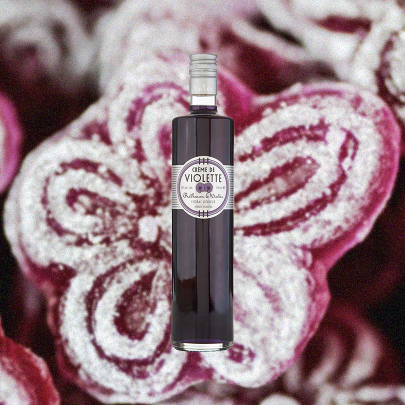 Bottle of Rothman & Winter Crème De Violette Liqueur over backdrop of purple candy.