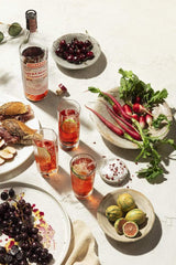 Table scape with Luxardo Sour Cherry Gin, cocktails, sandwiches, maraschino cherries, and root vegetables.