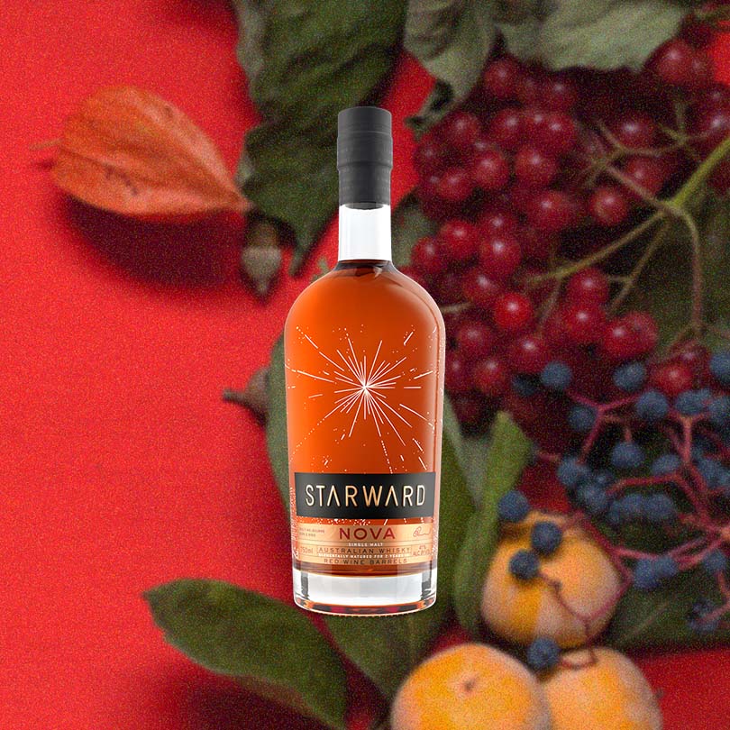 Bottle of Starward Nova Australian Single Malt Whisky, over blurred background of red berries, blueberries and peaches.
