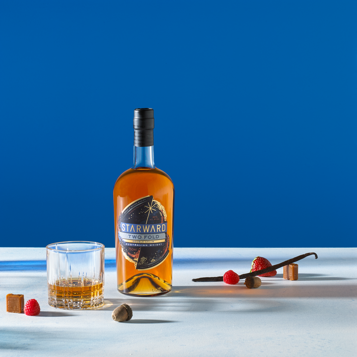 Bottle of Starward Two-Fold Whisky next to a neat pour and scattered fruits and candies.