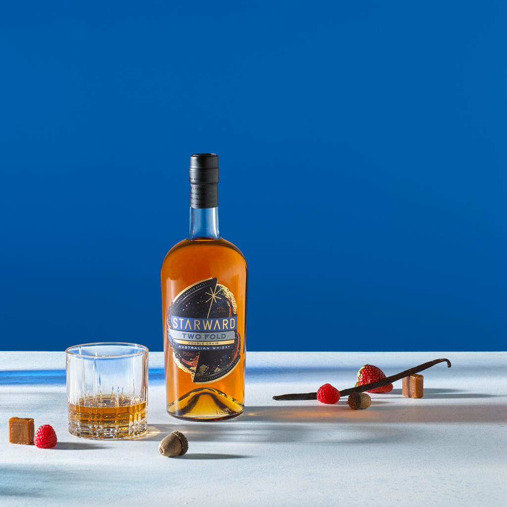Bottle of Starward Two-Fold Whisky next to a neat pour and scattered fruits and candies.