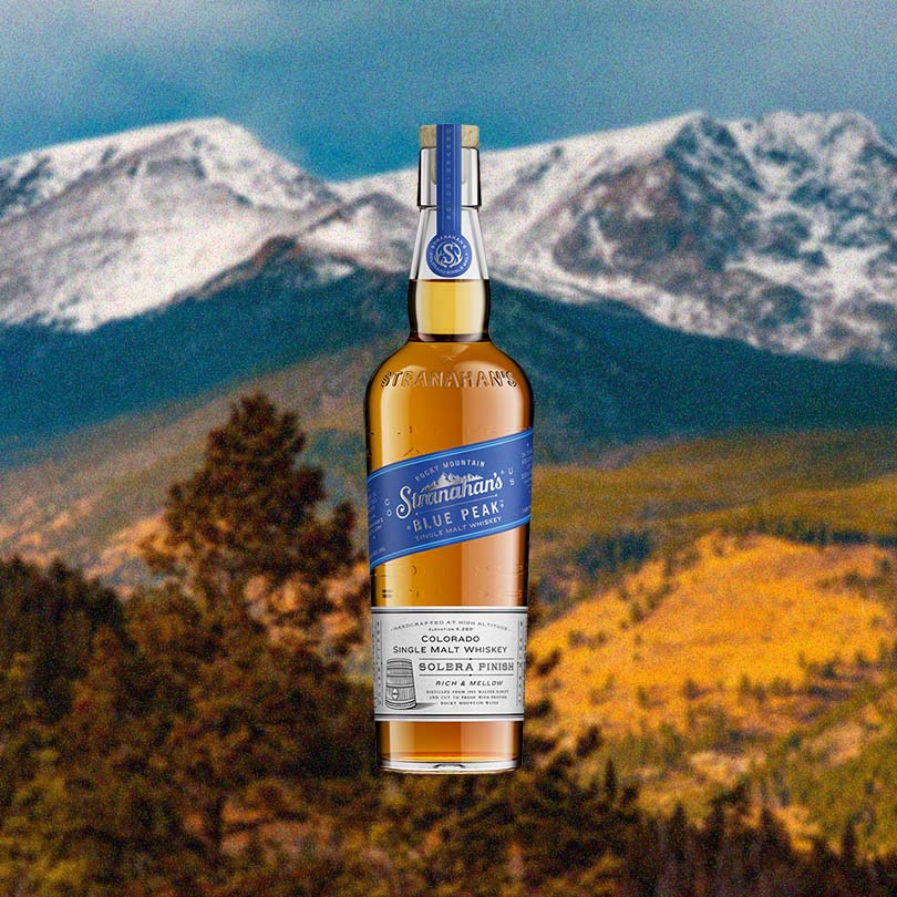 Bottle of Stranahan’s Blue Peak Colorado Single Malt Whiskey over backdrop of mountains.