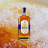 Bottle of Uncle Nearest Straight Rye Whiskey over background image of frothy beer.