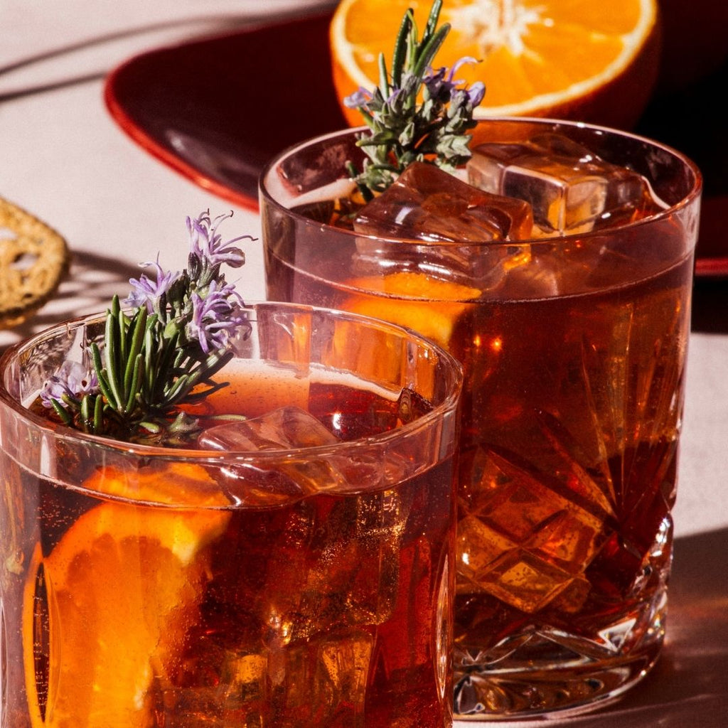 Two Negroni cocktails garnished with an orange slice and herbs.