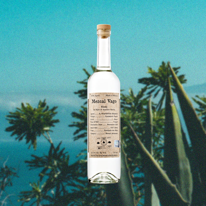 Bottle of Mezcal Vago Elote over backdrop of green plants, trees and the sky.
