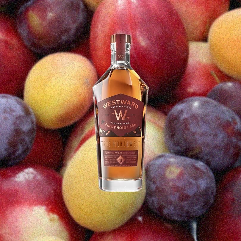 Bottle of Westward American Single Malt Whiskey Pinot Noir Cask, over a background of colorful fruits.