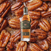 Bottle of Westward American Single Malt Whiskey Stout Cask, over close-up background of baked pecans.