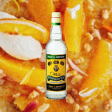 Bottle of Wray & Nephew White Overproof Rum over backdrop of orange candy, fruit medley.