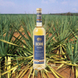 Bottle of Bottle of Xicaru Mezcal Reposado over backdrop of agave field.