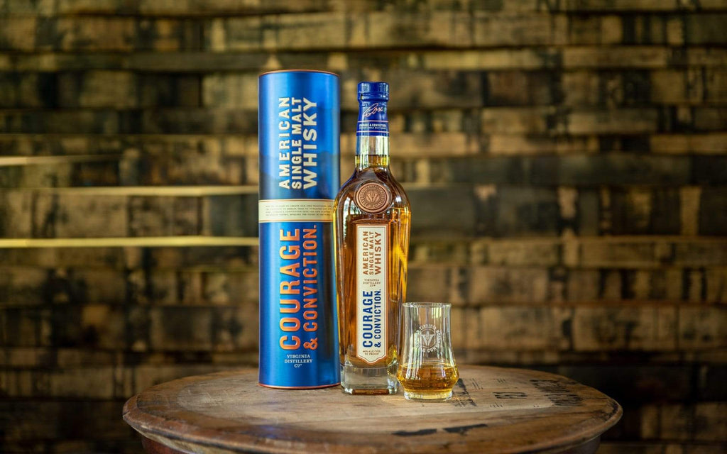 Bottle of Courage & Conviction American Single Malt Whisky on a wooden table next to a neat pour of the spirit.
