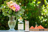 Bottle of Barr Hill Gin outside on table next to flowers and light cocktail.
