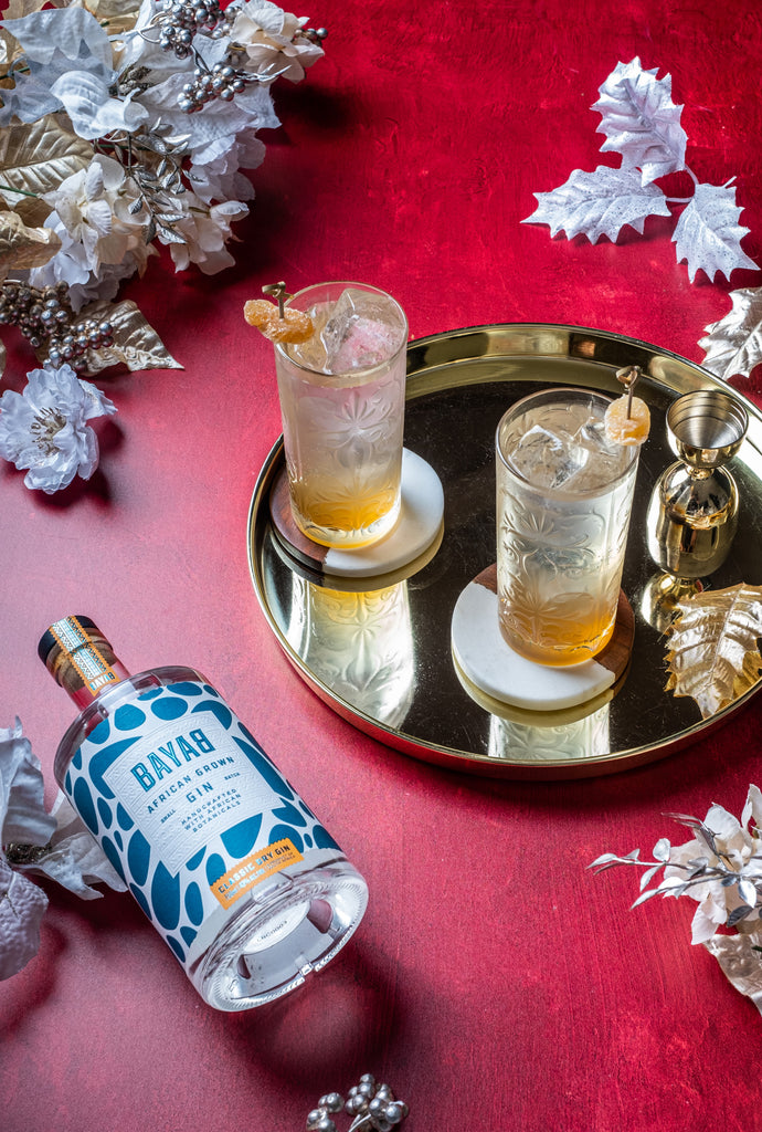 Bottle of Bayab Classic Dry Gin on a red table with 2 cocktails decorated for the holidays.