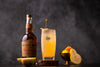 Bottle of Black Dirt Apple Jack Apple Brandy Bottled In Bond on a table next to a yellow cocktail.