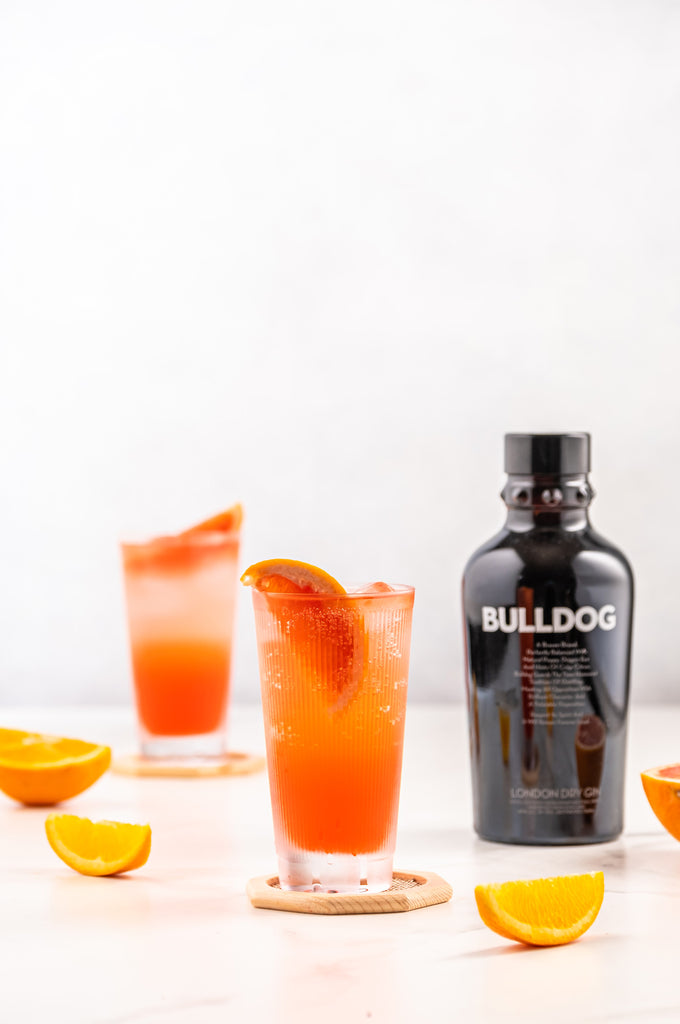 Bottle of Bulldog London Dry Gin on a marble table next to an orange cocktail glass.