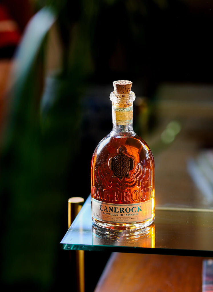 Bottle of Canerock Spiced Rum in dark lighting on the corner of a table.