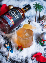 Bottle of Chairman's Reserve Spiced Rum laying down next to a cocktail, fake snow and small toys.