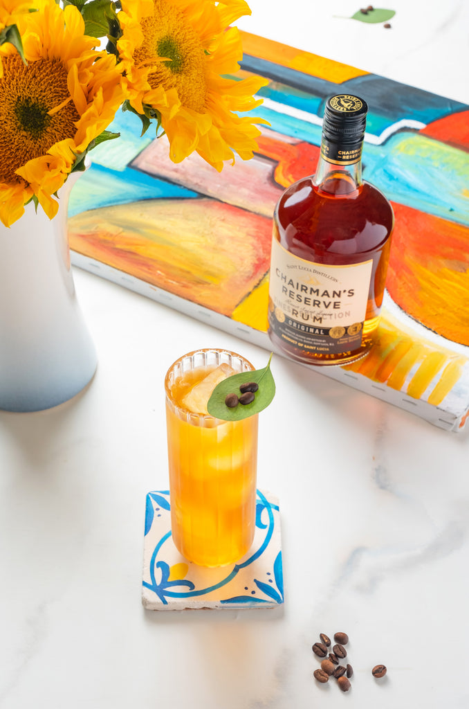750ml bottle of Chairman's Reserve Original Rum on a table next to flowers, art and a cocktail.