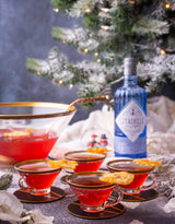 750ml bottle of Citadelle Gin on a table next to 4 cocktails and a Christmas tree.