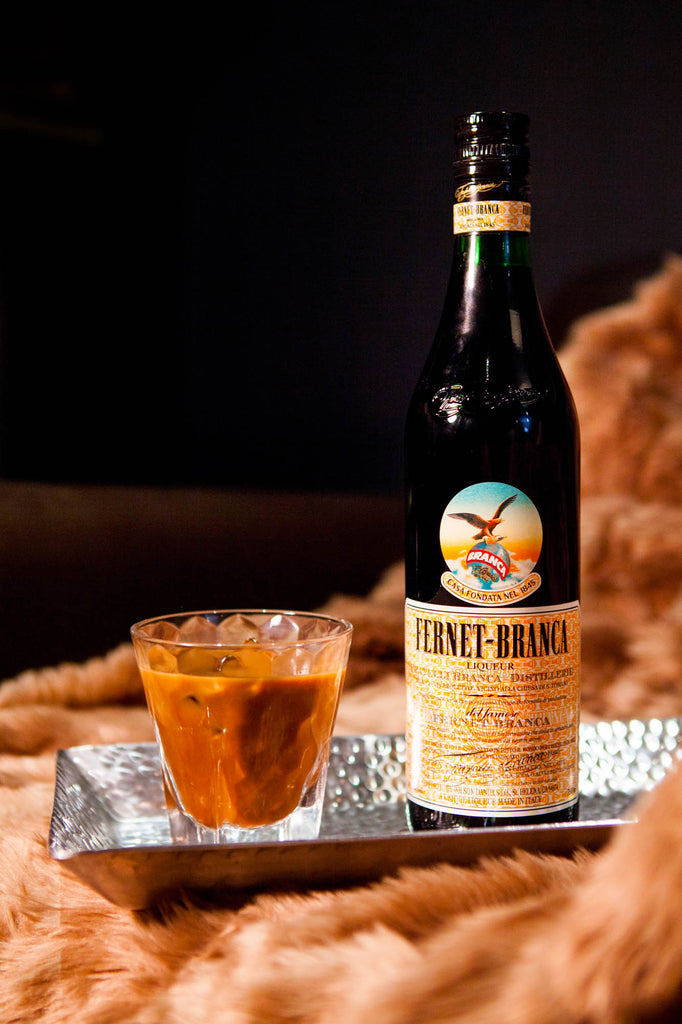 Bottle of Fernet-Branca Amaro Liqueur on a fur blanket next to a cocktail.