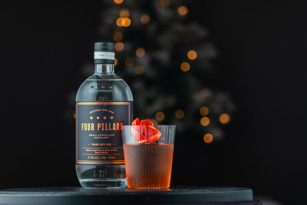 Bottle of Four Pillars Rare Dry Gin on a small table next to a cocktail garnished with a rose.