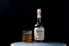 Bottle of George Dickel Superior Recipe No. 12 Whiskey on a table in front of a black background next to a simple cocktail.