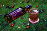 Bottle of Glenmorangie Lasanta 12 Year Scotch, lying on green grass, with a cocktail next to it and surrounded by multi-colored acorns.