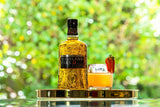 Bottle of Highland Park 12 Year Old Viking Honour Single Malt Scotch on a gold tray next to a light cocktail garnished with a strawberry.