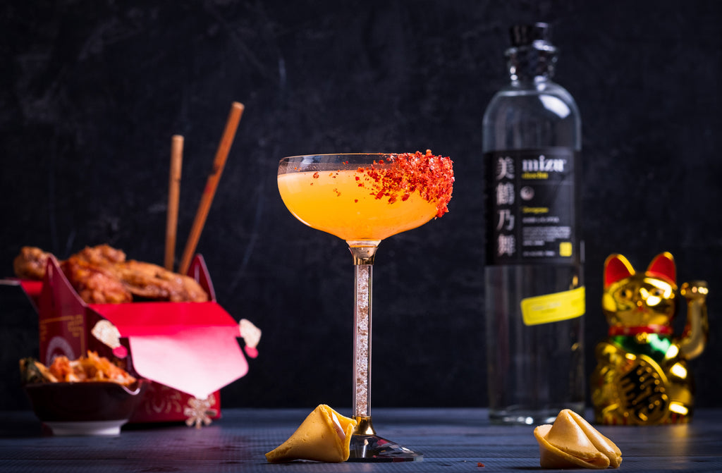 Orange cocktail on table with fortune cookies and bottle of Mizu.