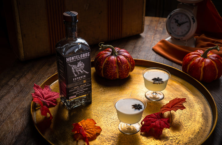 Well edited Bottle of Montelobos Espadin Mezcal Joven. on a gold tray next to two beautiful cocktails.